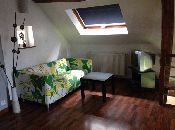 A small, cozy room with a sloped ceiling, a sofa with a floral pattern, a small table, a radiator, and a television. - House with Pool For even more fun. (Provency)