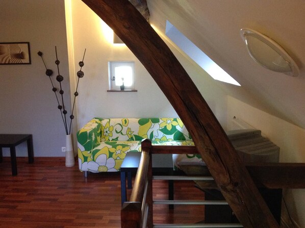 Ein Loft-Zimmer mit einer Holztreppe, einem grün-weißen Blumensofa, einem kleinen Tisch und einer Dekorationsvase.