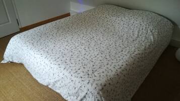 Ein Bett mit floralem Überwurf in einem Zimmer mit Holzboden und einer weißen Tür.