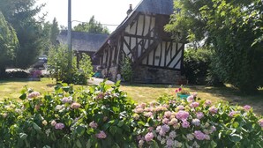 A traditional half-timbered house with a stone wall and a garden with pink hydrangea flowers.