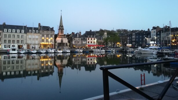 A waterfront view with a church steeple, boats, and buildings reflecting on the water.