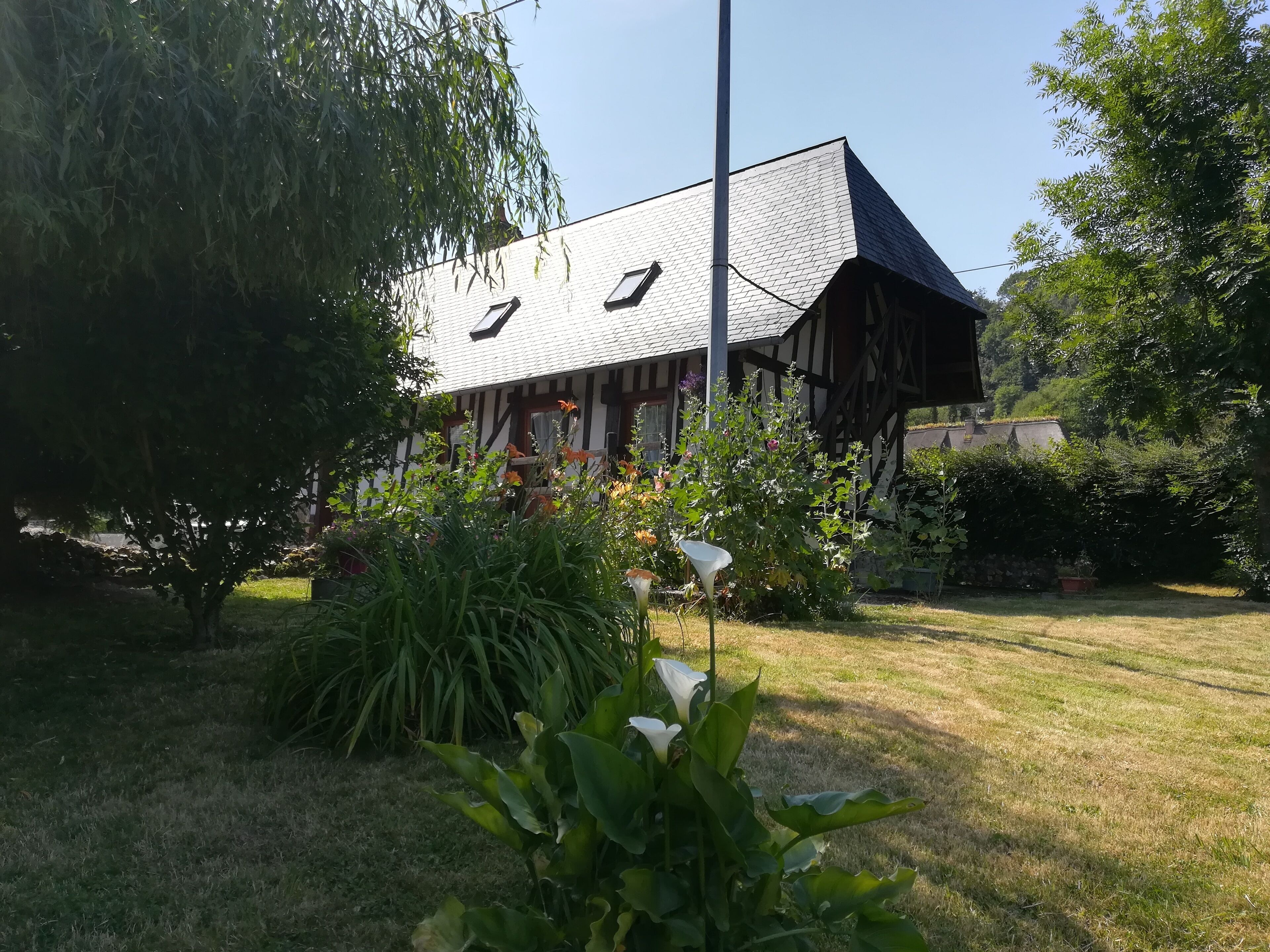 Un bâtiment traditionnel doté d’un toit en pente, entouré d’une végétation luxuriante et de plantes en fleurs.
