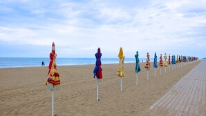 A beach with rows of colorful umbrellas lined up on the sand, a wooden boardwalk, and the ocean in the background.