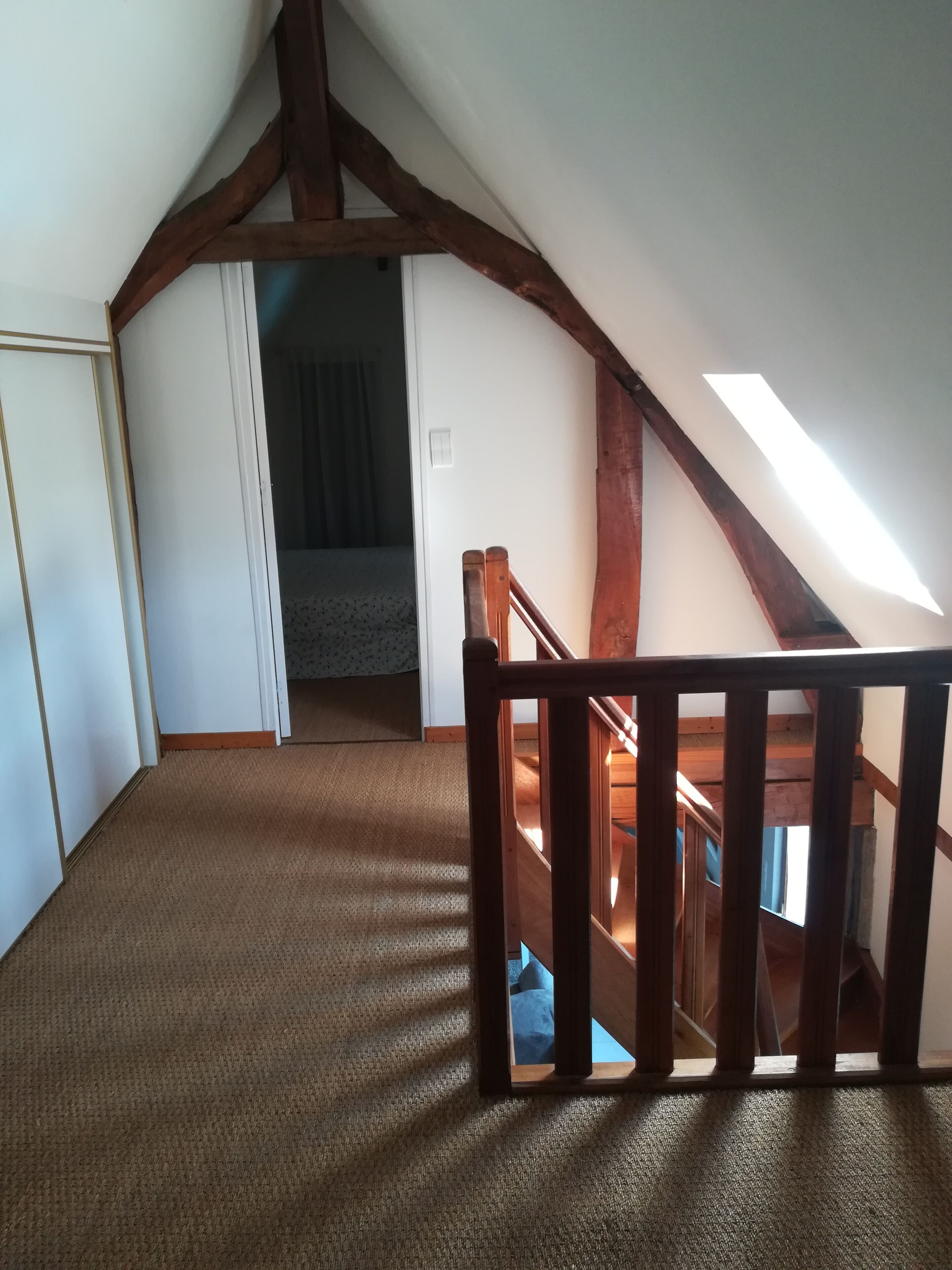 Ein Zimmer mit schrägen Wänden, Holzbalken, Teppichboden und Blick durch eine offene Tür.