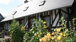 A traditional half-timbered house with a sloped roof, dormer windows, and a garden with flowering plants.