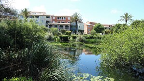 A serene pond surrounded by lush greenery and multi-story buildings with balconies. - Very beautiful T2 on the ground floor with trees, swimming pool, sea view, shops and beach  (Six-Fours-les-Plages)