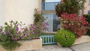 A residential building with a balcony, a concrete planter with purple flowers, and a green bush. - Very beautiful T2 on the ground floor with trees, swimming pool, sea view, shops and beach  (Six-Fours-les-Plages)