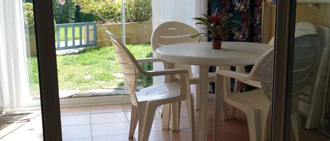 A patio with a round table and four chairs, a potted plant, and a view of a garden with a no parking sign.