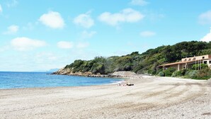 A beach with a building on a hill, a clear sky, and calm sea. - Very beautiful T2 on the ground floor with trees, swimming pool, sea view, shops and beach  (Six-Fours-les-Plages)