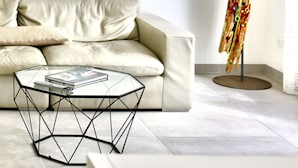 Un salon moderne avec un canapé beige, une table basse en verre, une sculpture abstraite aux couleurs vives et un tableau représentant des voiliers.