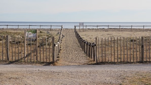 Un chemin de gravier mène à une plage, et de chaque côté se trouve une clôture en bois.