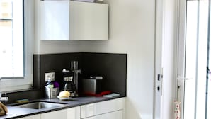 Une cuisine moderne avec des meubles blancs, un plan de travail noir et une horloge au mur.