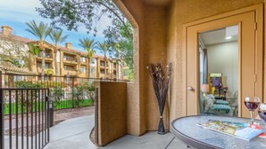 A balcony with a table, a door, and a view of a building with balconies and palm trees. - Quiet 1st Floor, Gated, Pool, Wi-Fi, Free Parking, Gym (Phoenix)