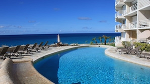 Ein Pool mit geschwungener Kante, Liegestühle und Blick aufs Meer.