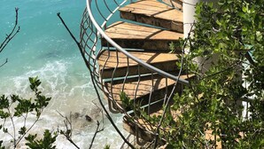 Eine Wendeltreppe führt zu einem Balkon mit Blick auf das türkisfarbene Meer.