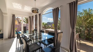 A modern dining area with a glass table and black chairs, large windows with curtains, and a view of the outdoors. - Luxury Villa del Duque in Chayofa, dream location, private pool, sea views, golf (Chayofa)