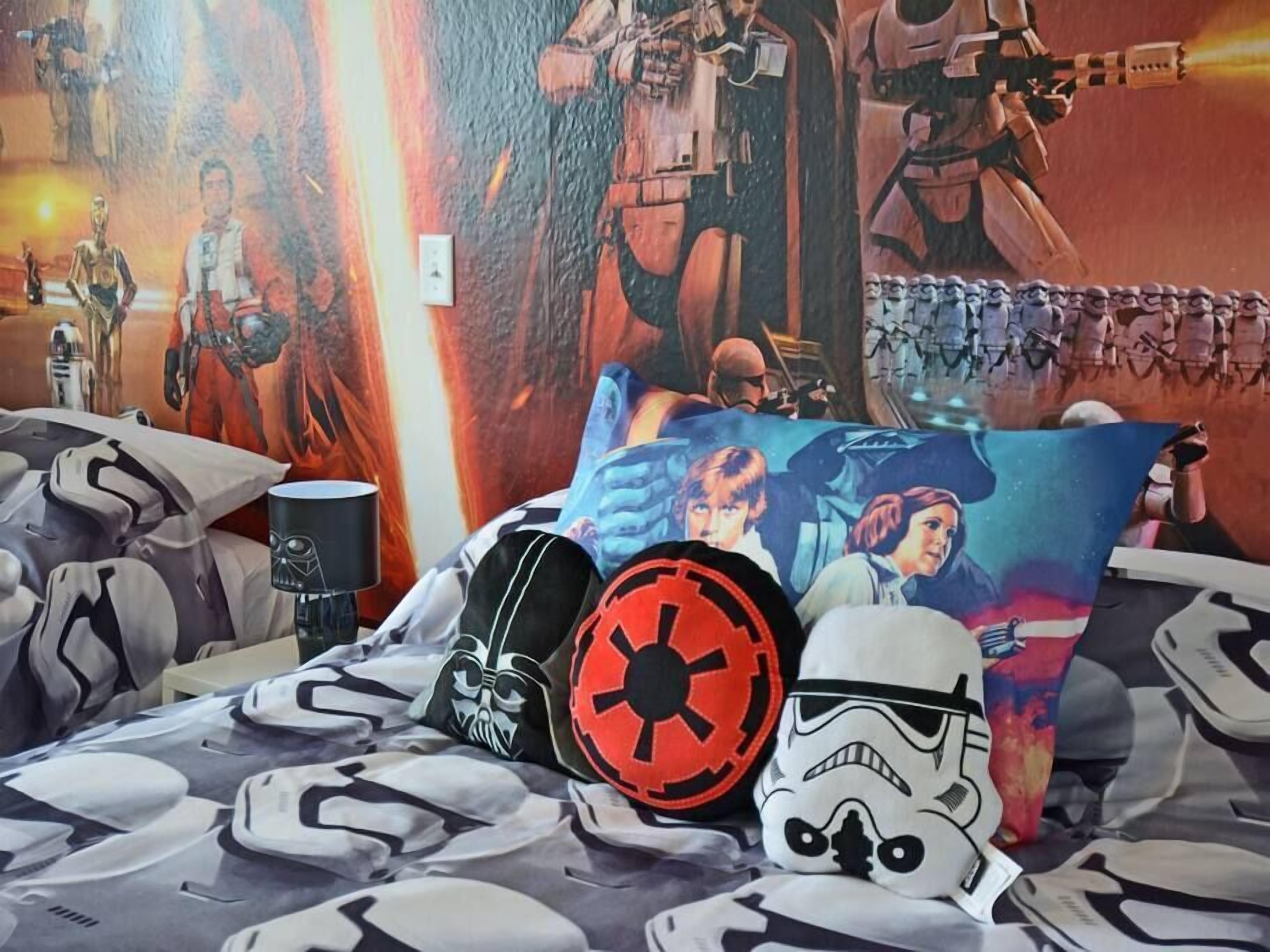 A bedroom with Star Wars themed bedding and pillows, including a large poster of characters and a Stormtrooper helmet.