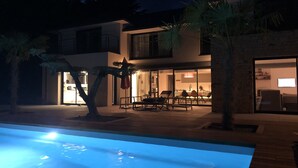 Une maison moderne à deux étages, dotée d’une piscine, d’un espace extérieur aménagé et d’un intérieur bien éclairé.