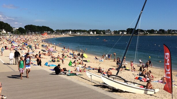 Een druk strand met mensen die zonnebaden en zwemmen.
