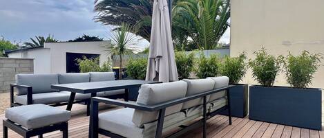 An outdoor patio with a wooden deck, grey cushioned seating, and a large umbrella.