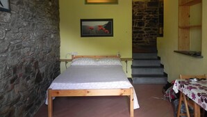 Un dormitorio con cama de madera, pared de piedra, una escalera y un cuadro en la pared.