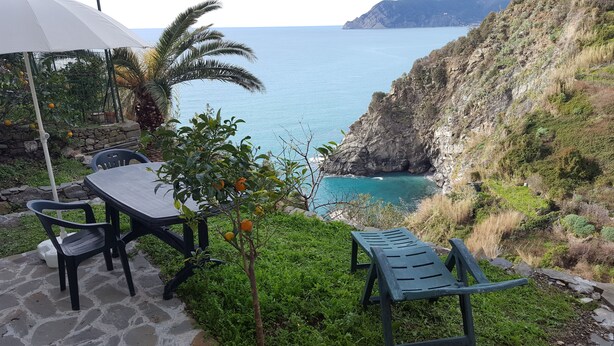 Un patio con una mesa, sillas, una sombrilla blanca y vistas al mar y a los acantilados.