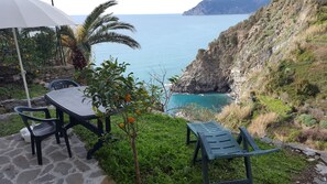 Um pátio com mesa e cadeiras, um guarda-sol branco e vista para o mar e falésias.