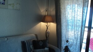 Una sala de estar con sofá, lámpara y ventana con cortinas.