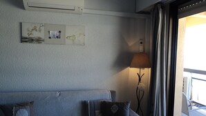 Una habitación con un sofá gris, una lámpara y un ventanal con cortinas.