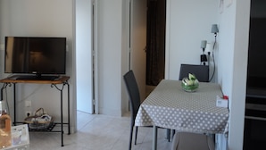 Una habitación pequeña y limpia con una televisión sobre un mueble bajo, una mesa de comedor con mantel de lunares y una silla.