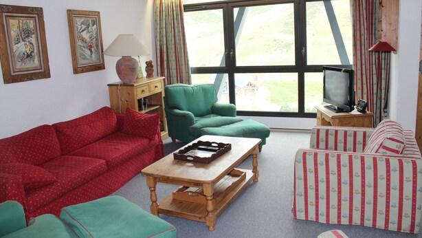 A living room with a red sofa, green armchair, striped sofa, wooden coffee table, and a television on a wooden stand.