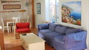 A living room with a wooden ceiling, a red sofa, a blue sofa, a white cabinet, and a painting of a coastal scene. - Hidden Villa- A Hidden Paradise with beautiful furnished garden patio (San Diego)