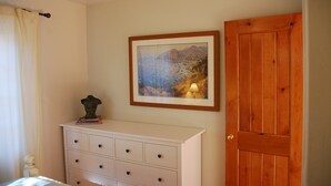 A bedroom with a white dresser, a framed landscape painting, and a wooden door. - Hidden Villa- A Hidden Paradise with beautiful furnished garden patio (San Diego)