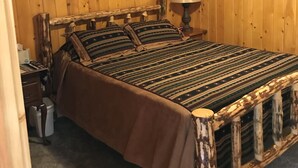 Una habitación con paneles de madera, una cama, una mesita de noche, una lámpara y una ventana con cortinas.
