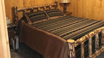 A wooden-paneled room with a bed, a nightstand, a lamp, and a window with curtains.