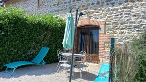 Un edificio de piedra con una puerta de madera y una ventana. Hay una mesa y sillas afuera, y un paraguas verde cuelga de un mástil.