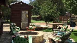 Ein rustikaler Sitzbereich im Freien mit Steinböden, Holzmöbeln und einer kleinen Holzkonstruktion.