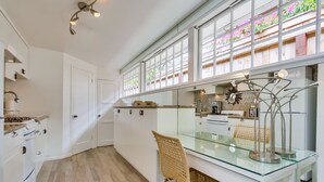 A modern kitchen with white cabinetry, a glass dining table, and a wicker chair. - Sandcastle Hideaway, Dog Friendly, Designer Studio, Private Patio And Parking! (La Jolla)