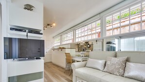 A modern kitchen with a flat-screen TV, a dining area with a glass table, and a sofa with decorative pillows. - Sandcastle Hideaway, Dog Friendly, Designer Studio, Private Patio And Parking! (La Jolla)