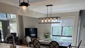 A modern kitchen with a large island, a dining area with a chandelier, and a TV in the background. - Palmetto Dunes-Golf-Pickleball-Tennis- Beach! (Hilton Head Island)