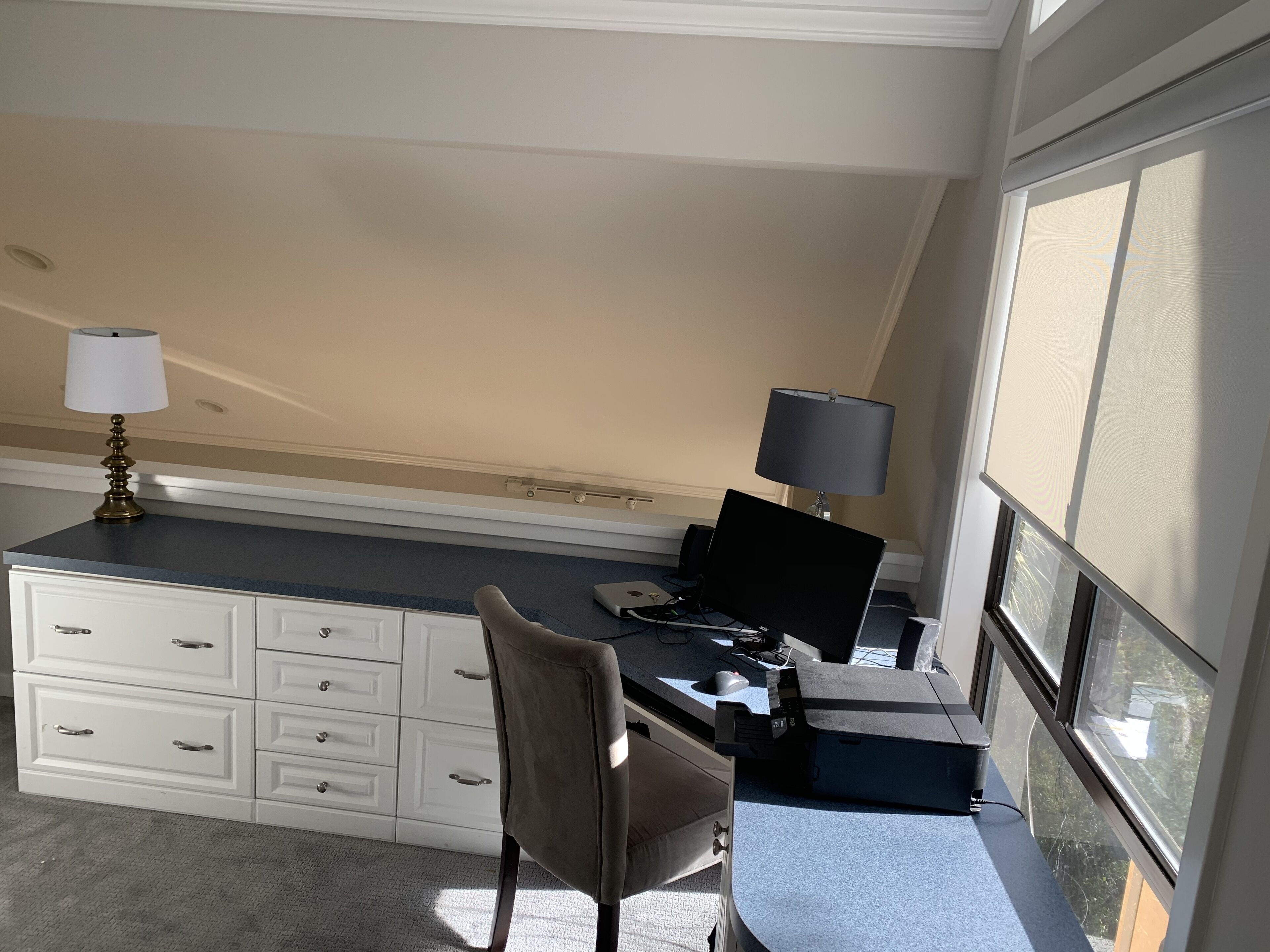 A small, well-lit room with a desk, chair, and two lamps. There is a window providing natural light and a view of the outside.
