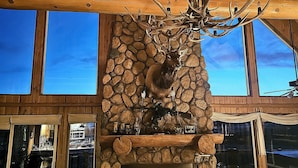 Un interior rústico con chimenea de piedra, vigas de madera y una escultura de cabeza de ciervo.