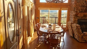 Un comedor con una mesa grande y sillas, una chimenea de piedra y vistas panorámicas a través de las ventanas.