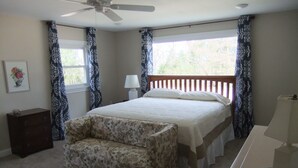 Een slaapkamer met een bed, nachtkastje, dressoir, stoel, plafondventilator en een raam met gordijnen.