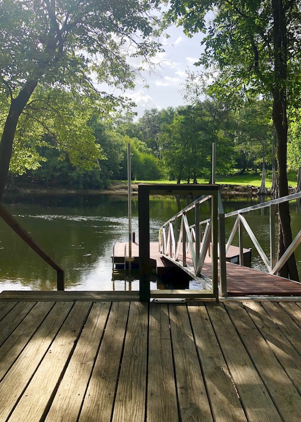 A wooden dock extending over a calm river, surrounded by lush green trees.