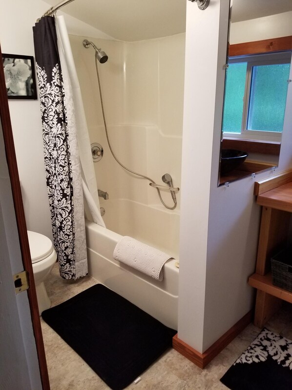 A bathroom with a bathtub, shower, toilet, and a window.