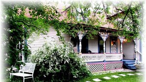 A white house with a porch, a bench, and a garden.