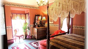 A bedroom with a four-poster bed, a dresser, a chair, and a chandelier.