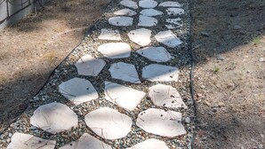 Un sendero de piedra que conduce a una cabaña con garaje, rodeada de altos pinos.