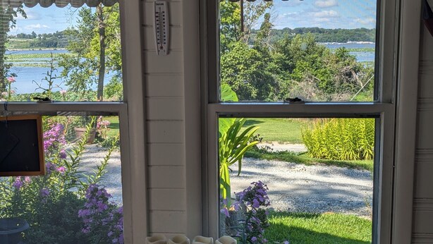Una stanza con una grande finestra che si affaccia su un lago e sulla vegetazione. Sul davanzale sono presenti elementi decorativi.